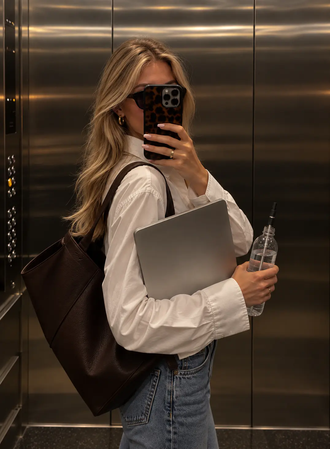 A woman holding a water bottle with a black Aelo Straw and a laptop in an elevator.